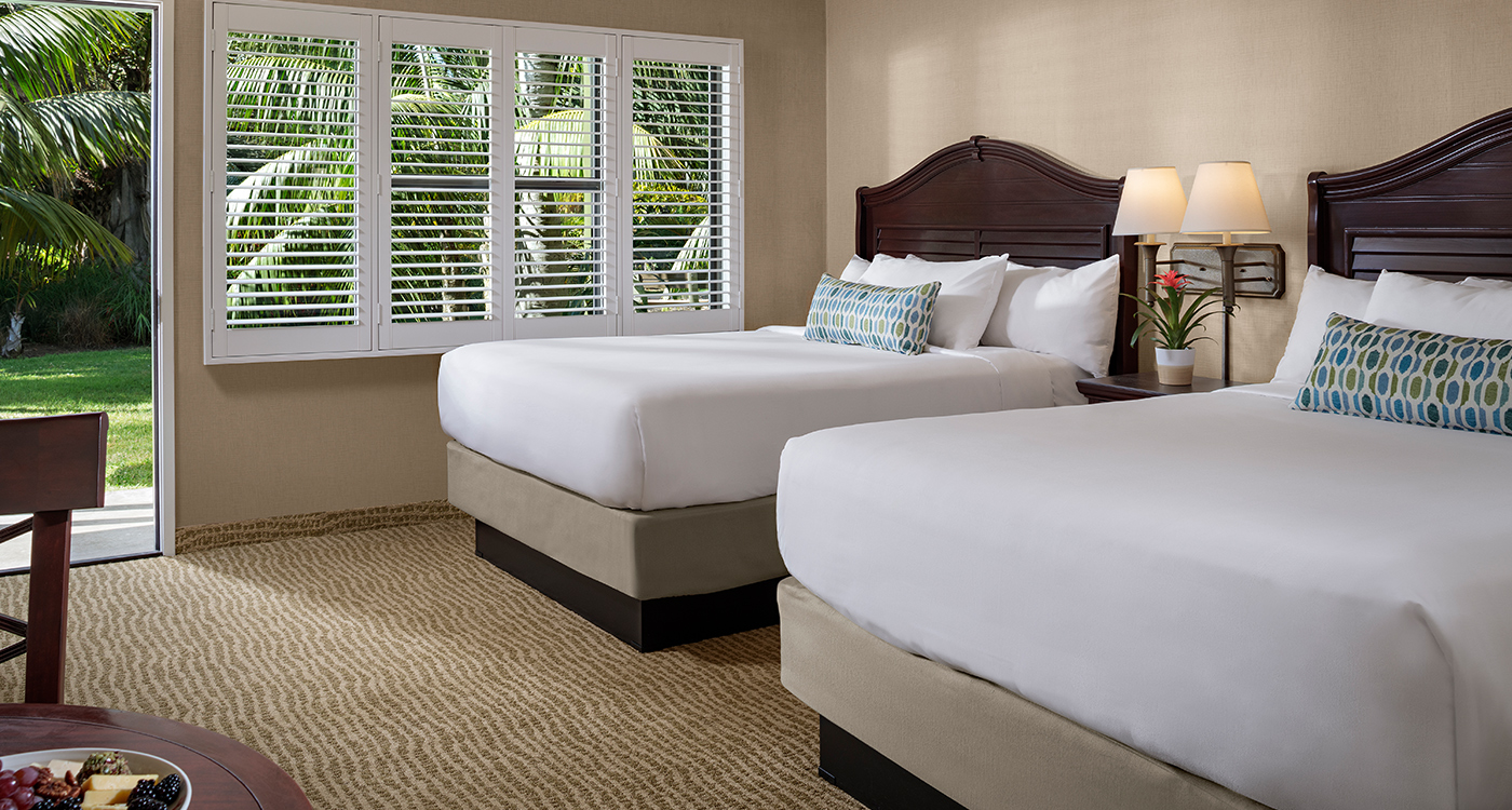 A hotel room with two twin beds, a window with blinds, and a view of the outdoors.
