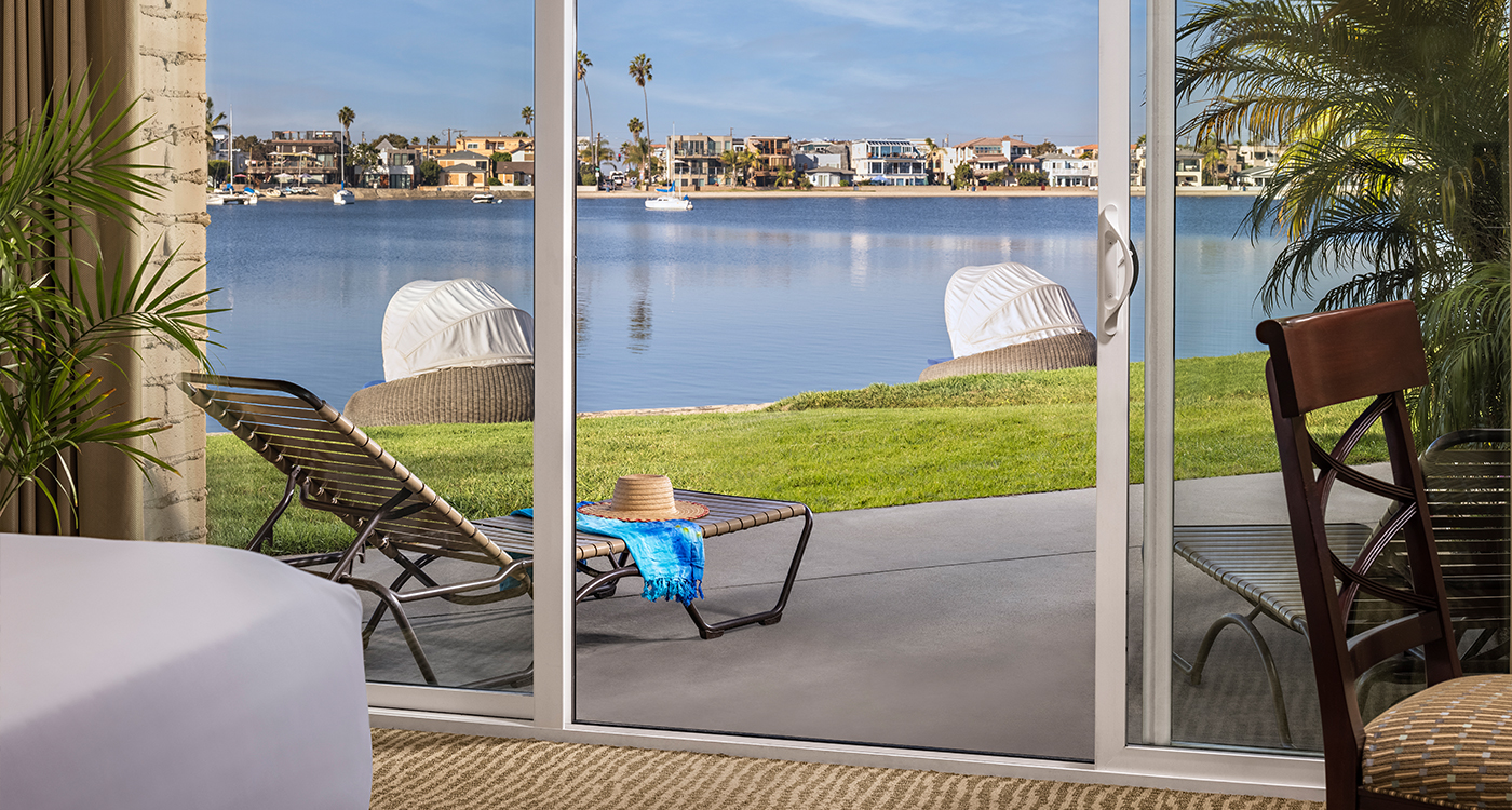 A beachfront room with a sliding glass door leading to a patio with a lounge chair and a table, overlooking the ocean.