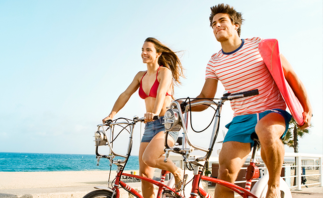 Couple riding bikes on Mission Bay, San Diego with Surfboards