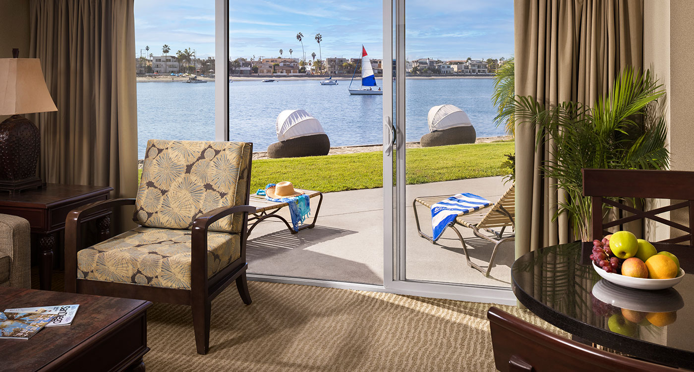 A room with a sliding glass door leading to a patio with a beach view.
