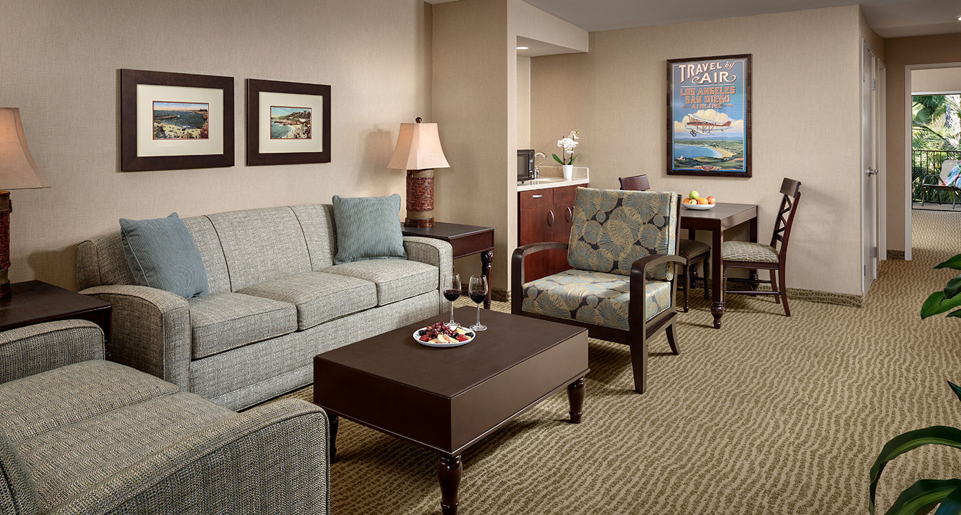A wide view of a suite's living area with a sofa, coffee table, dining table, and chairs.