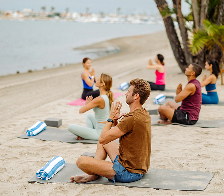 Co-workers experiencing yoga on the beach in Mission Bay, one of the many team building events at the Bahia Resort Hotel in San Diego.