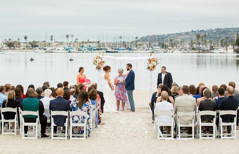 A beach wedding ceremony with guests seated on white chairs